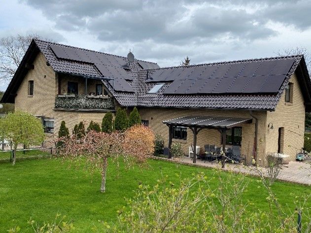 Ein großes Backsteinhaus mit schwarzem Dach und Solarzellen auf dem Dach.