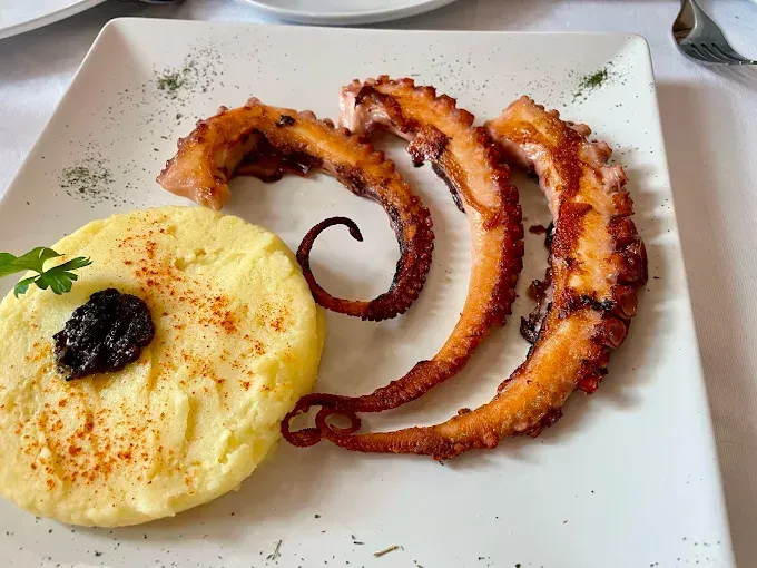 Un plato blanco cubierto con pulpo frito y puré de patatas.