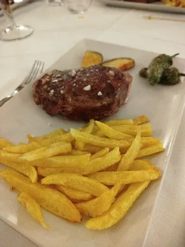 Un plato blanco cubierto con papas fritas y un filete sobre una mesa.