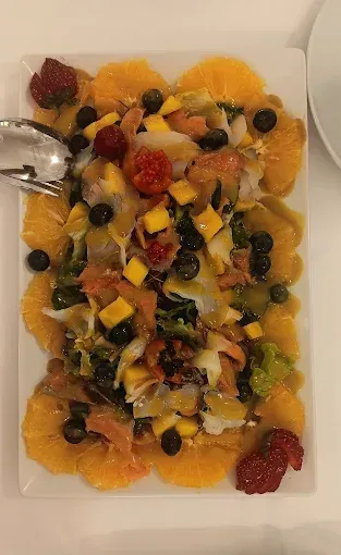 Un plato blanco cubierto con una ensalada de naranjas, bayas, aceitunas y salmón ahumado.