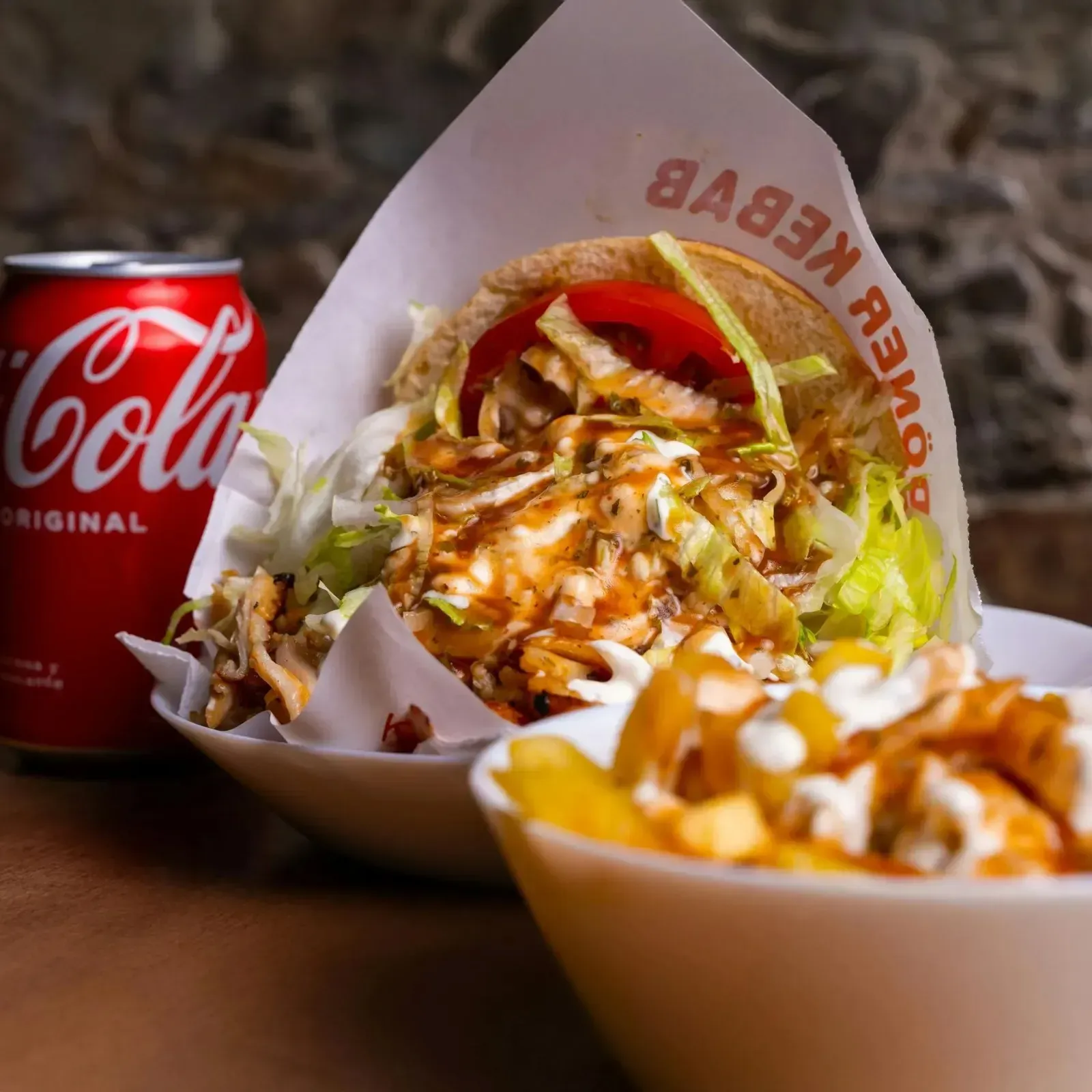 Sándwich de doner kebab, patatas fritas con salsa y una lata de Coca-Cola sobre una mesa.