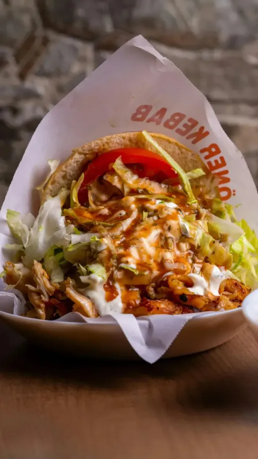 Döner kebab en pan pita con lechuga, tomate, salsa y carne sobre una envoltura de papel blanco.