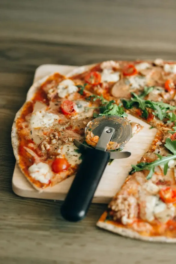 Pizza sobre tabla de madera con cortador de pizza, lista para servir, colocada sobre una superficie de madera.