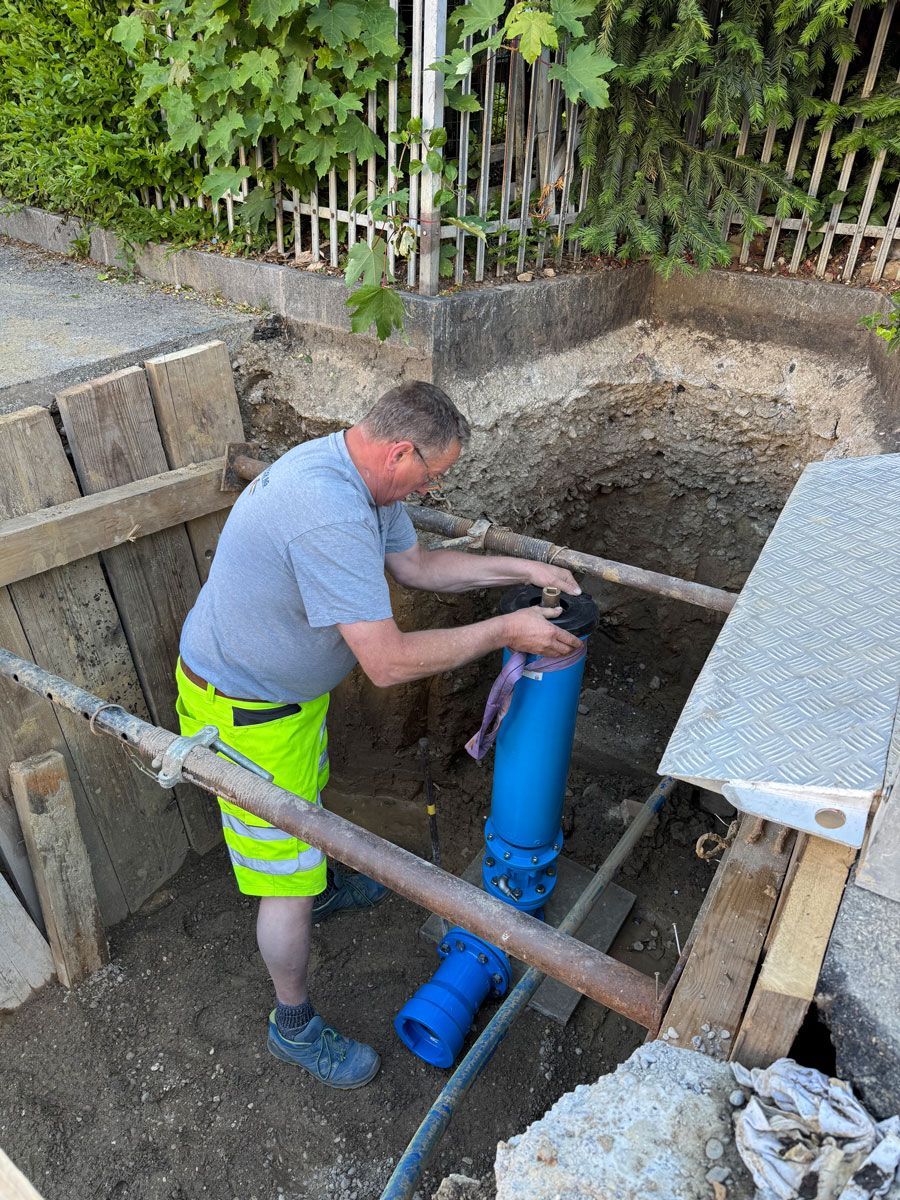 Arbeiter verlegt blaue Rohre in einem ausgehobenen Graben auf einer Baustelle