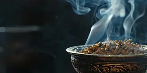 Un cuenco decorativo con incienso ardiendo que emite un tenue humo azul sobre un fondo oscuro.