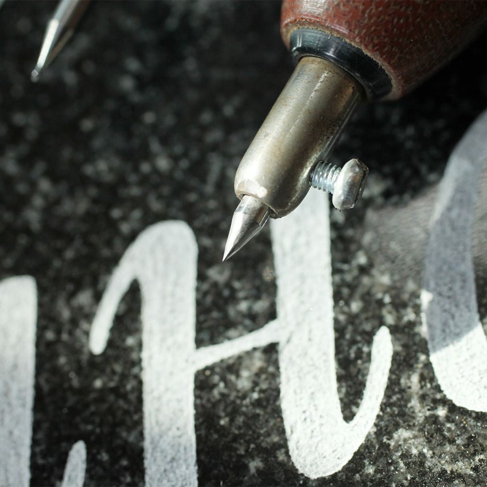 Valkoisten kirjaimien kaivertaminen mustaan ​​kivipintaan.