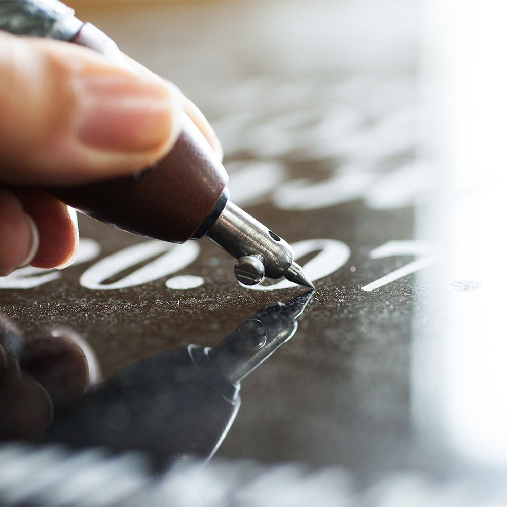 Päivämäärän kaivertaminen heijastavaan, tummaan kivipintaan.