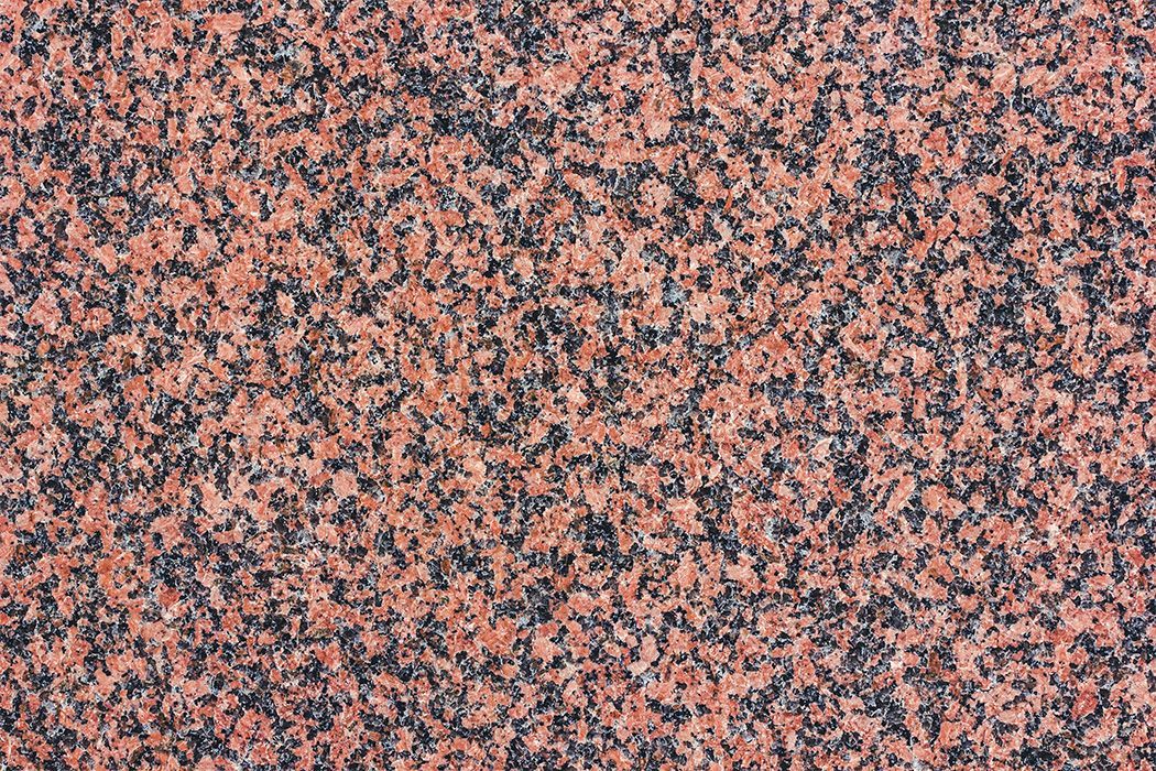 Lähikuva punaisesta ja mustasta täplikkäästä graniitista, jolla on tasainen rakenne.