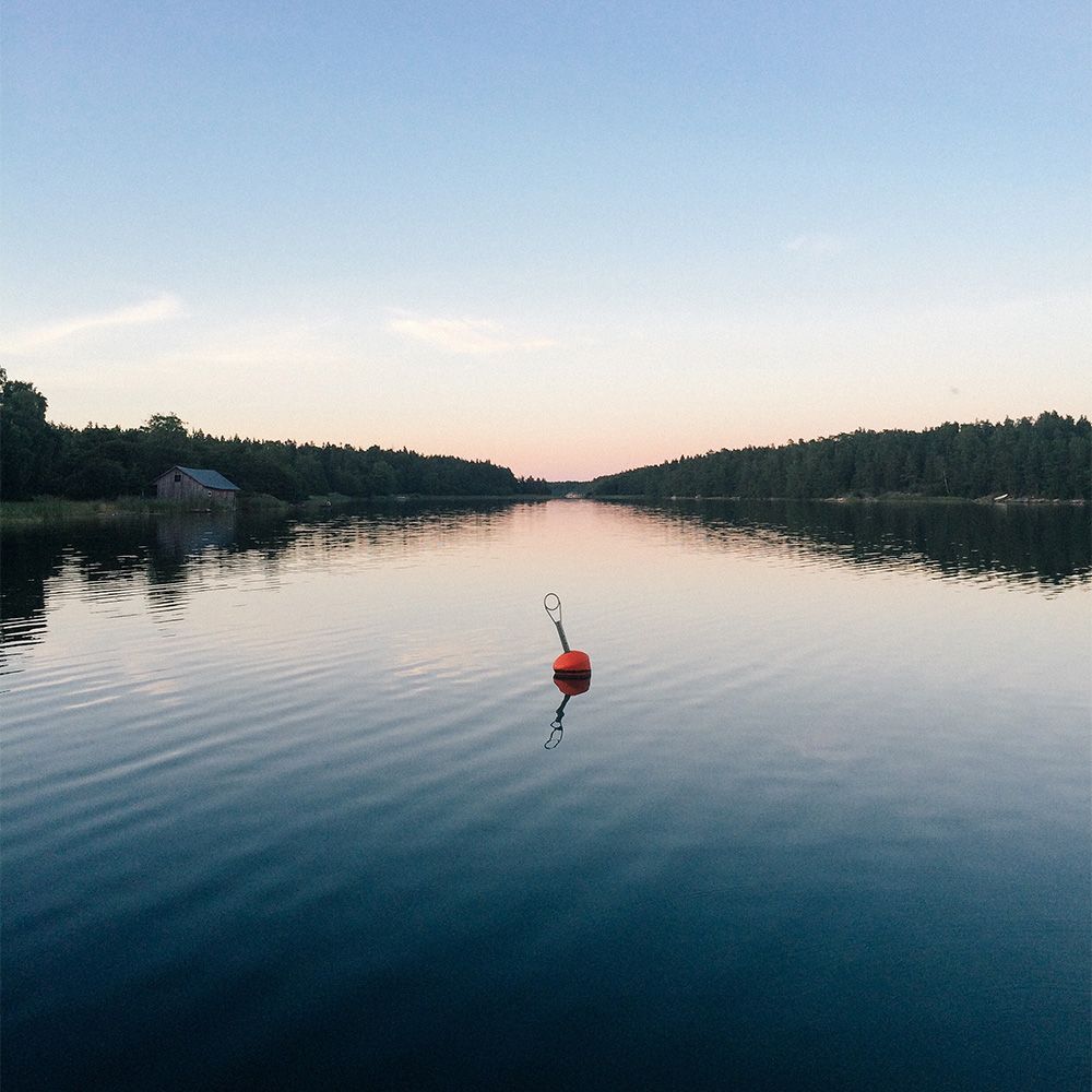 Oranssi poiju kelluu tyynen, sinisen järven keskellä auringonlaskun aikaan puiden reunustamien rantojen keskellä.