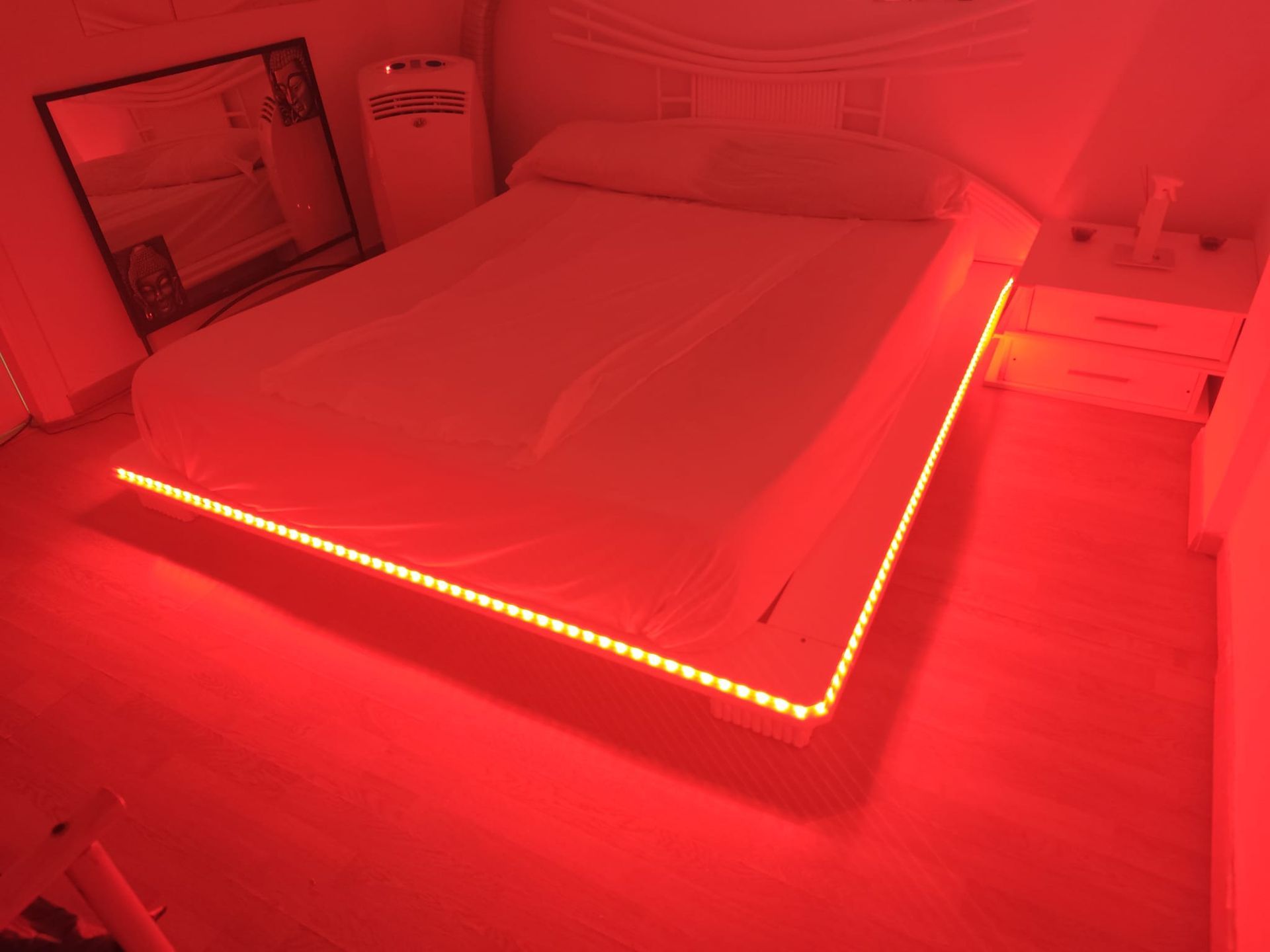 Cama en una habitación con tiras de luces LED rojas a lo largo del marco de la cama y una suave iluminación ambiental roja.