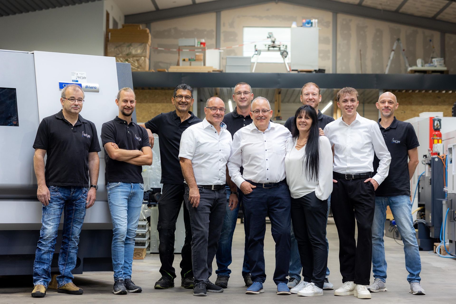 Eine Gruppe von zehn Personen posiert in einer Produktionsstätte für ein Foto.