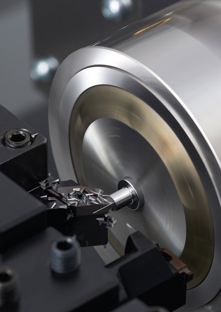 Eine Metalldrehmaschine bearbeitet ein zylindrisches Werkstück; Metallspäne sind sichtbar.