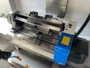 Eine CNC-Maschine hält einen Schraubstock auf einem Maschinentisch, seitlich befindet sich ein blauer Motor.