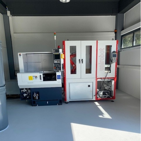 Innenansicht einer Maschinenwerkstatt mit CNC-Drehmaschine und automatisiertem Robotersystem.