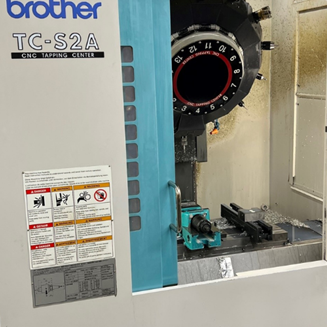 Brother TC-S2A CNC-Gewindeschneidzentrum mit geöffneter Tür, die den Werkzeugwechsler und den Arbeitsbereich zeigt.