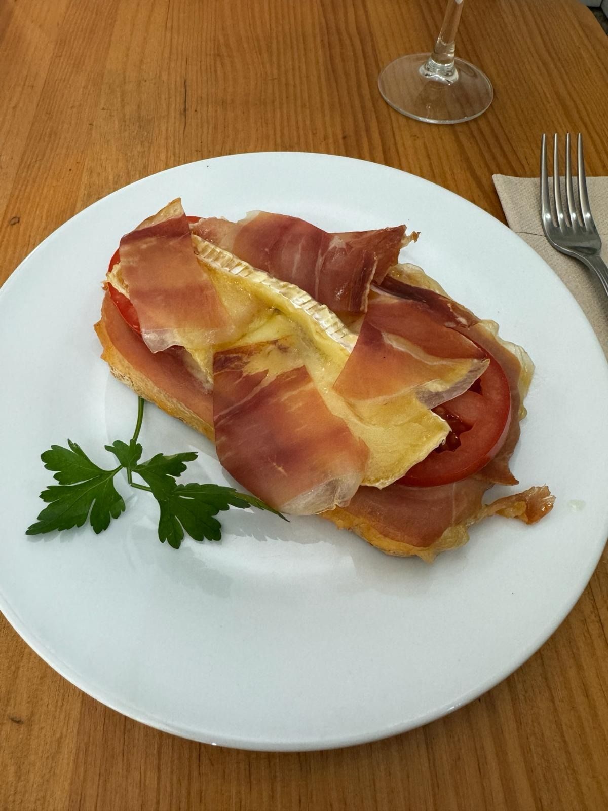 Un plato blanco cubierto con jamón, queso y tomates.