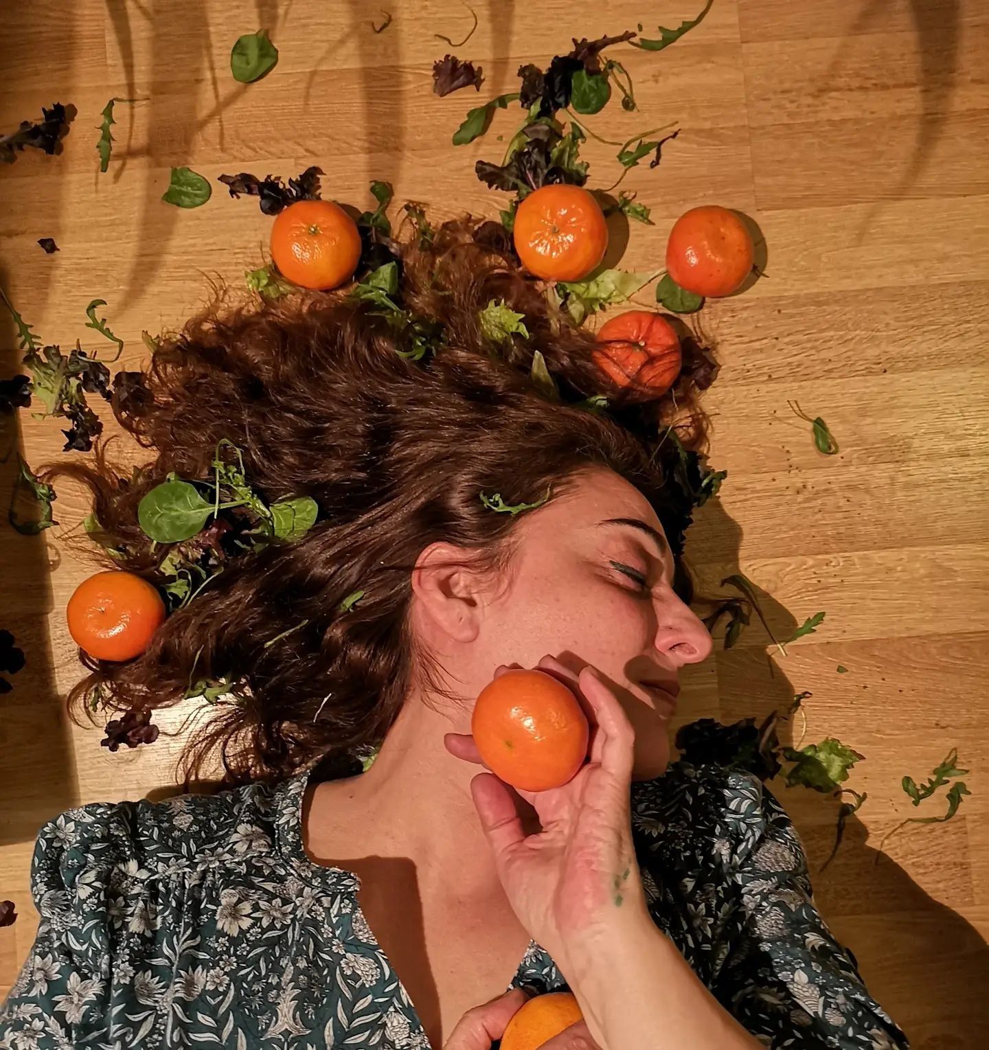 Una mujer tendida en el suelo con naranjas en el pelo.