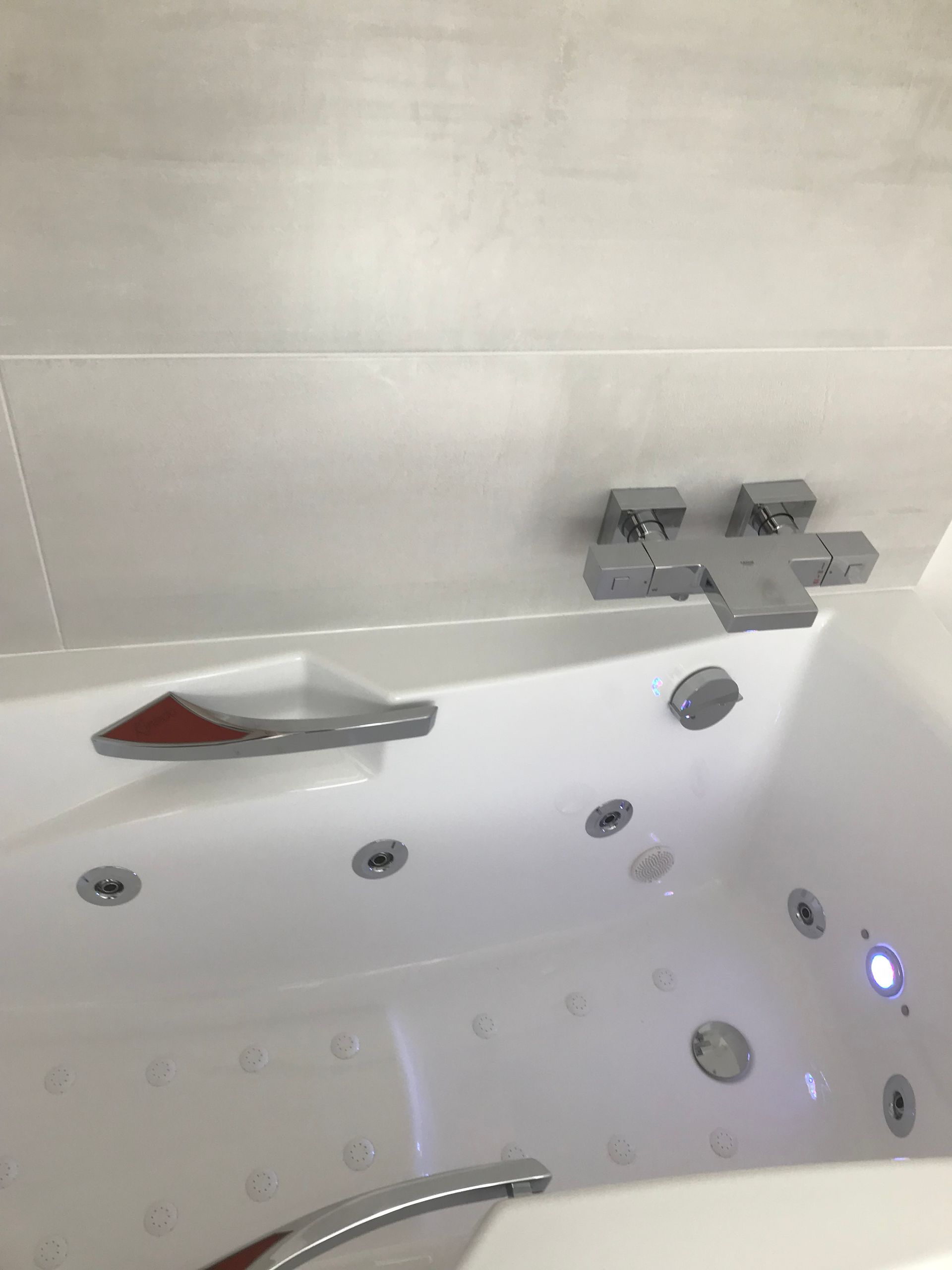 Baignoire d’angle blanche avec robinetterie chromée, jets et objet rouge flottant près du rebord