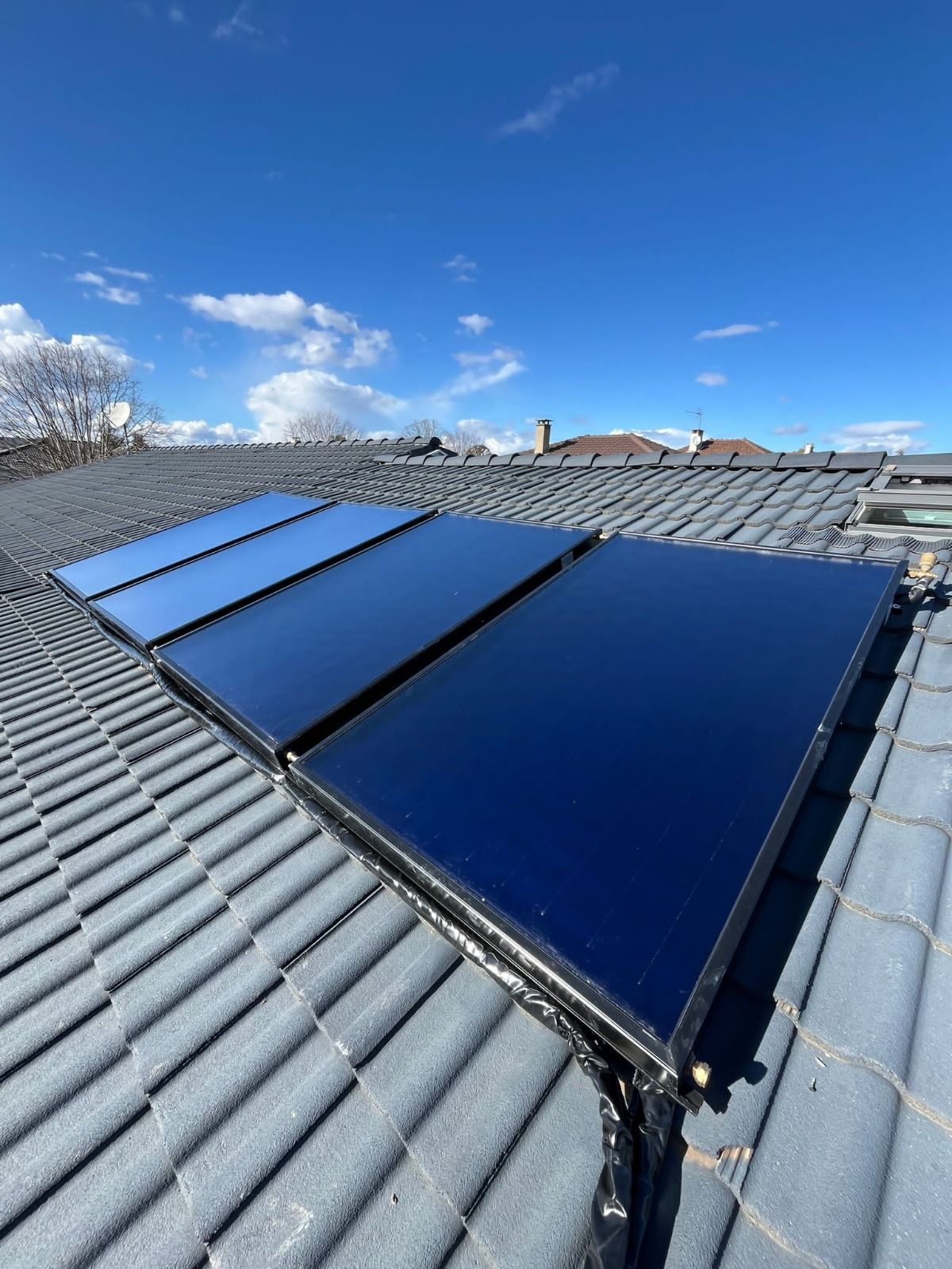 Maison avec panneaux solaires sur un toit de tuiles rouges, terrasse avec table et chaises, journée ensoleillée sous un ciel bleu.