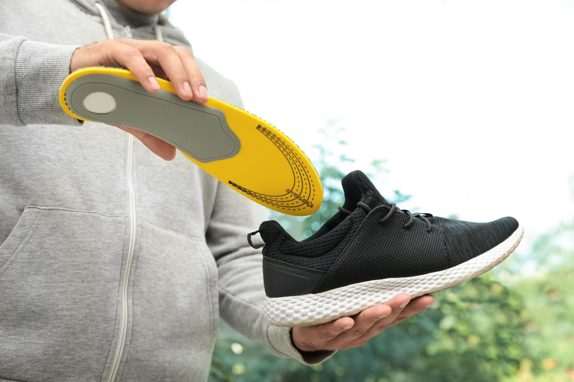 Eine Person hält ein Paar Schuhe und eine gelbe Einlegesohle.