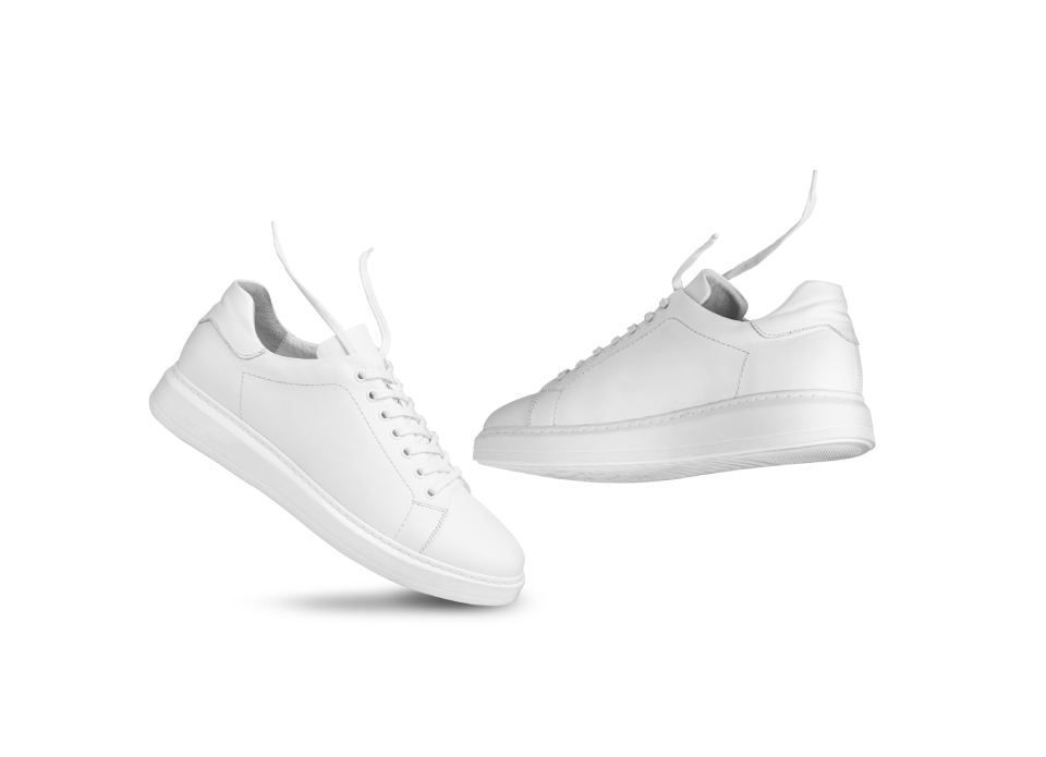 Ein Paar weiße Turnschuhe fliegen auf einem weißen Hintergrund durch die Luft.