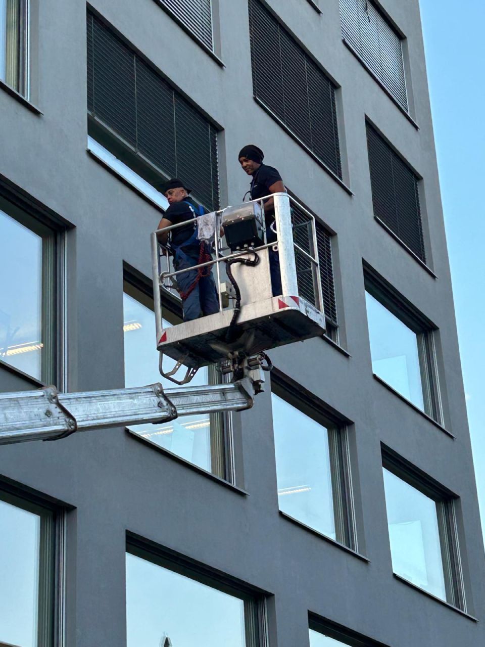 Zwei Personen arbeiten auf der Plattform eines Aufzugs an der Aussenfassade eines hohen Gebäudes.