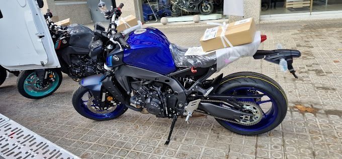 Una motocicleta azul está estacionada al costado de la carretera al lado de un camión blanco.