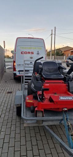 Una cortadora de césped roja está en un remolque al lado de una camioneta blanca.