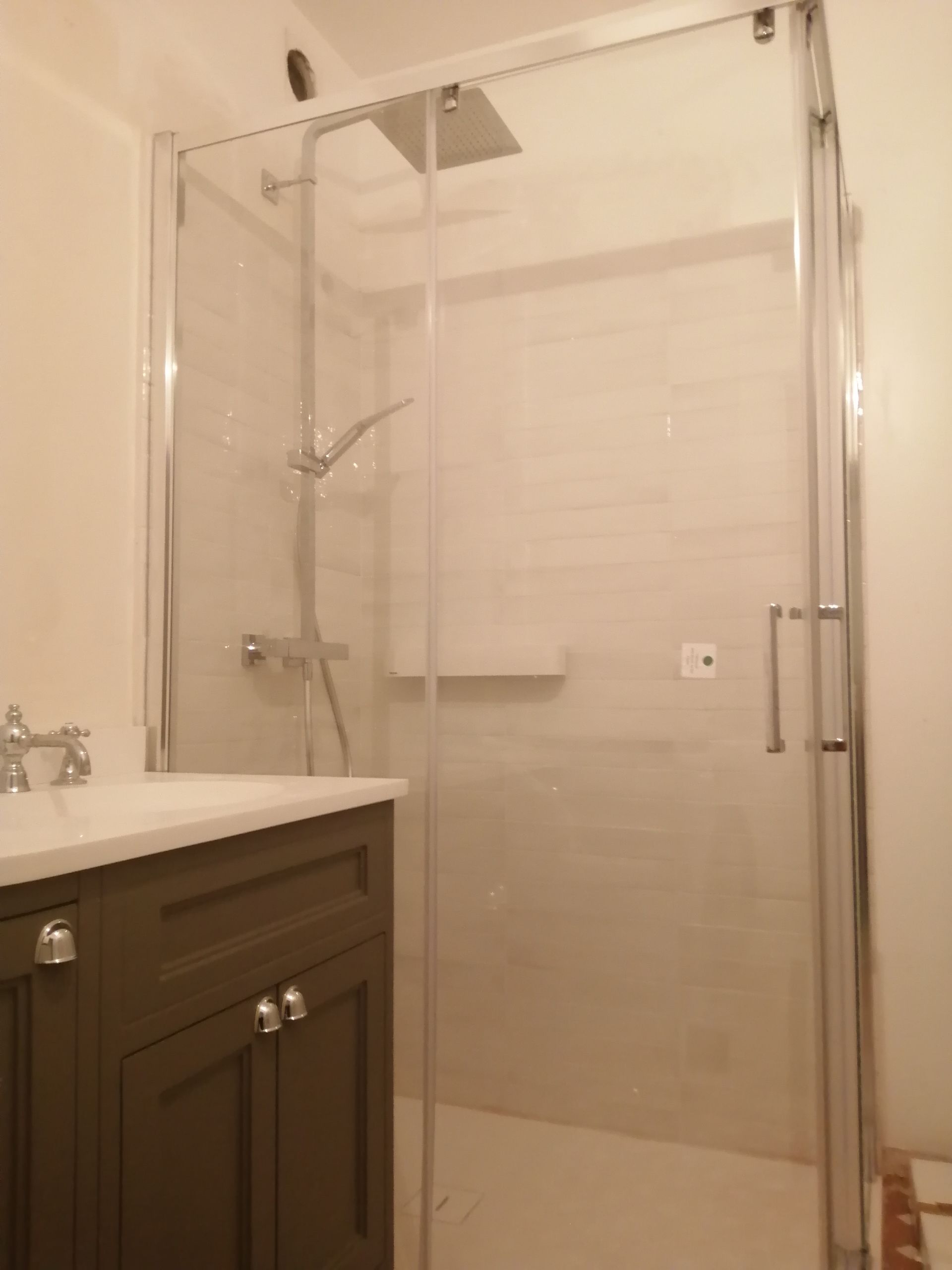 Installation d'une douche avec un receveur blanc, mitigeur thermostatique et pommeau carré, fixation paroi de douche fixe et d'une porte. Mur en carrelage. Installation meuble marron sous plan vasque blanc en céramique et robinetterie