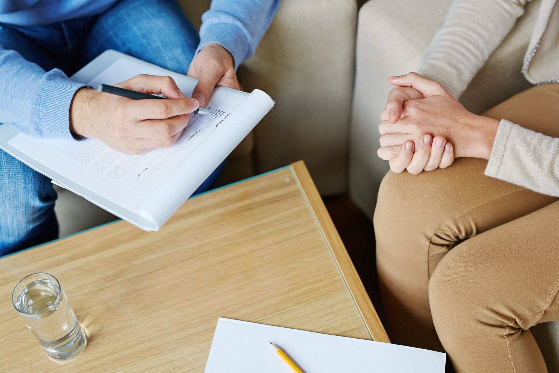 Terapeuta tomando notas mientras un paciente junta sus manos, en un ambiente tranquilo.