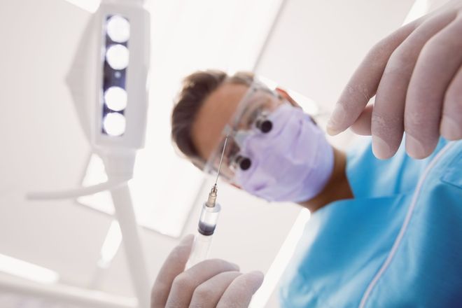 Dentista con mascarilla y guantes examinando la cámara con instrumentos dentales bajo las brillantes luces de la clínica.