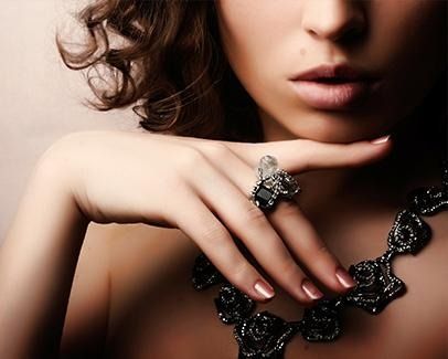 Primer plano de una mujer que lleva un collar y un anillo negros con joyas, con la mano cerca de los labios.