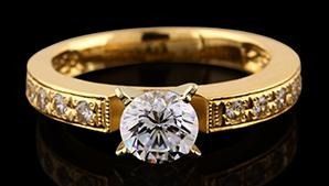 Anillo de oro con un gran diamante redondo central y diamantes más pequeños a lo largo de la banda sobre un fondo negro.