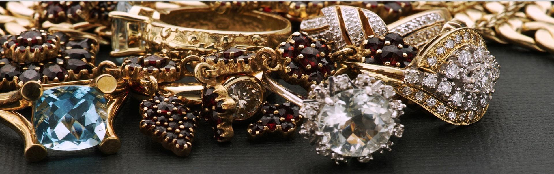Anillos y pulseras de oro y piedras preciosas surtidos sobre una superficie oscura.