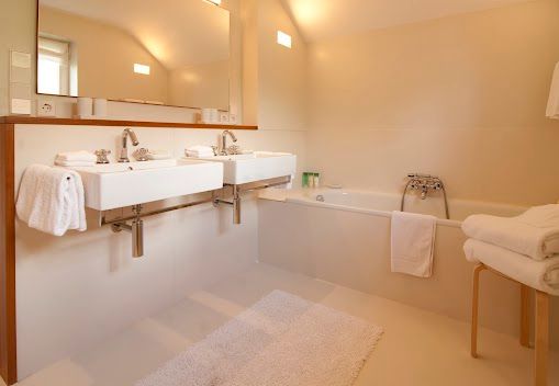 Badezimmer mit zwei Waschbecken, einer Badewanne und weißen Handtüchern. Beige Wände und weißer Boden.