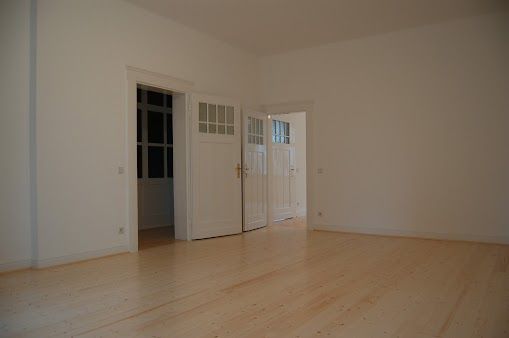 Leerer Raum mit hellen Holzböden, weißen Wänden und zwei weißen Türen.