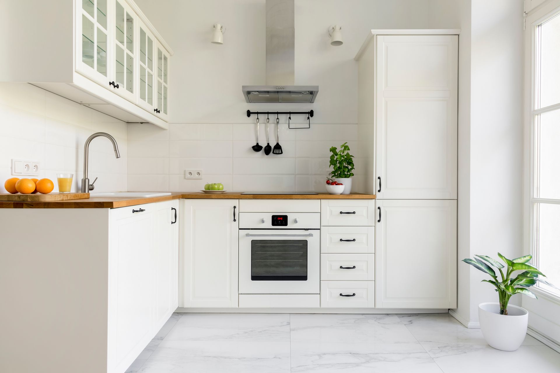 Cuisine moderne et lumineuse d'un blanc éclatant avec comptoirs en bois, four encastré, placards et plantes en pot.
