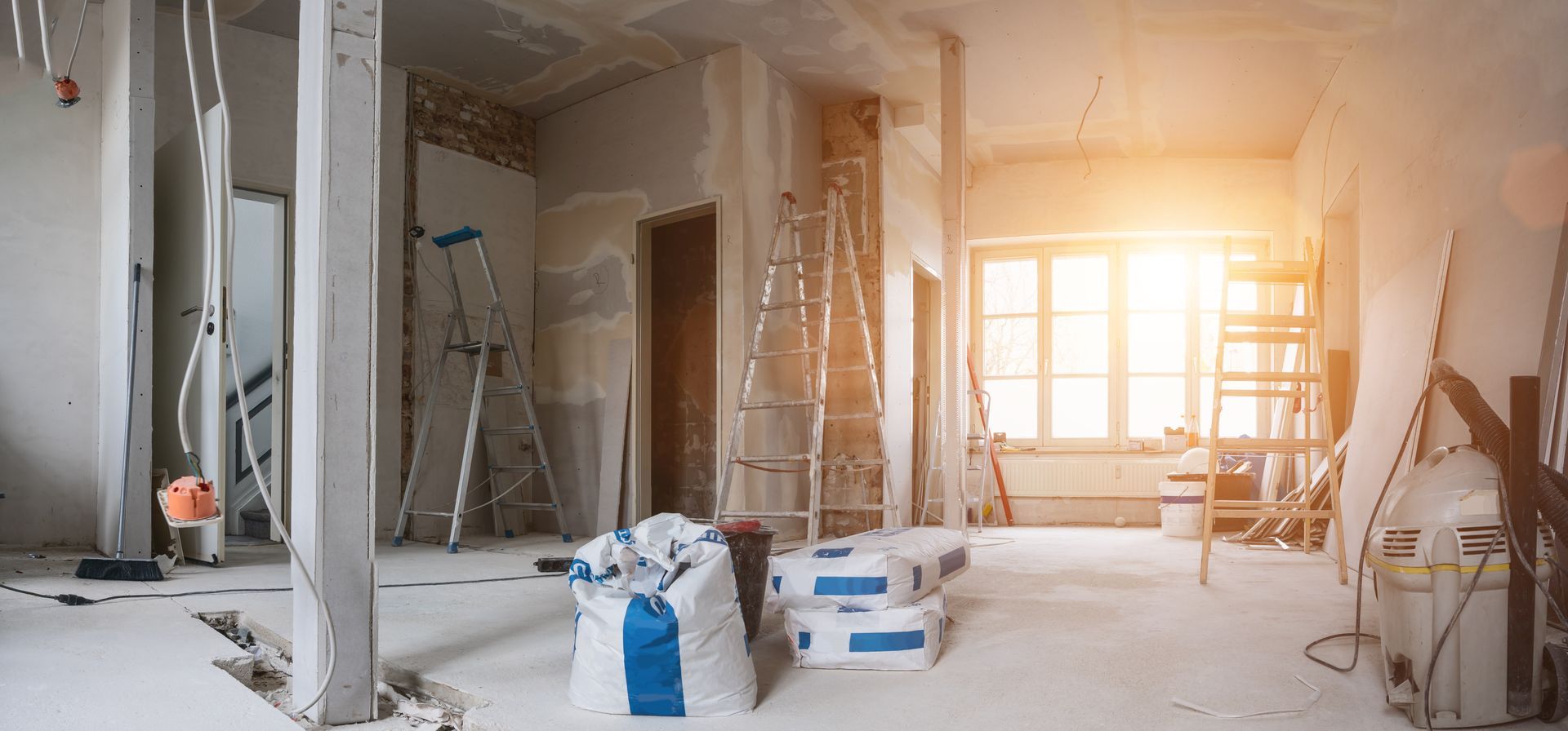 Pièce ensoleillée en cours de rénovation avec échelles, outils, plaques de plâtre et matériaux de construction