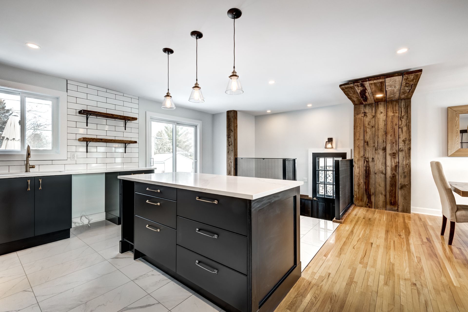 Cuisine moderne avec armoires noires, îlot blanc, suspensions lumineuses et parquet.