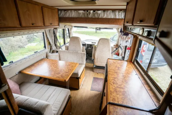 Interior de un RV que muestra un área de comedor, asientos y gabinetes de almacenamiento.