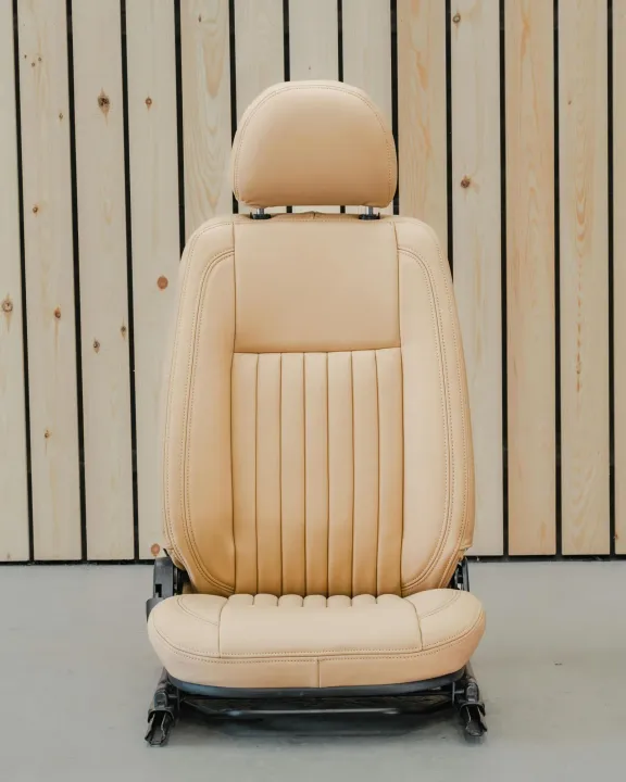 Asiento de coche de piel beige con reposacabezas, sobre un fondo de paneles de madera.