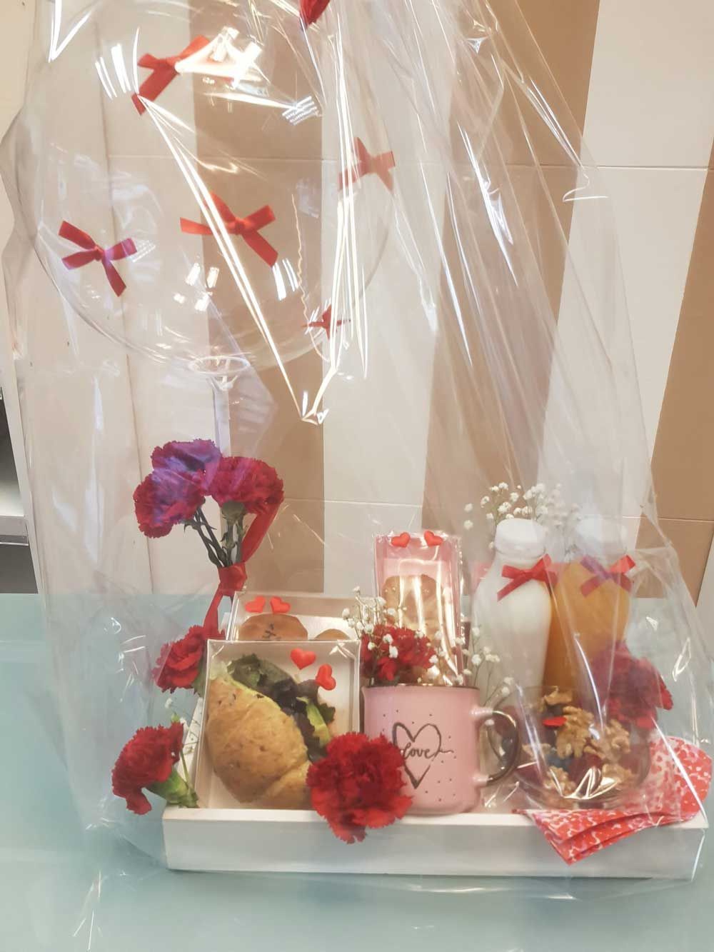 Una bandeja llena de comida y flores está envuelta en plástico.