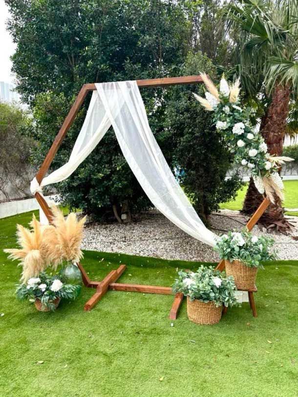Un arco de madera decorado con flores y hierbas de la pampa se encuentra sobre un exuberante campo verde.