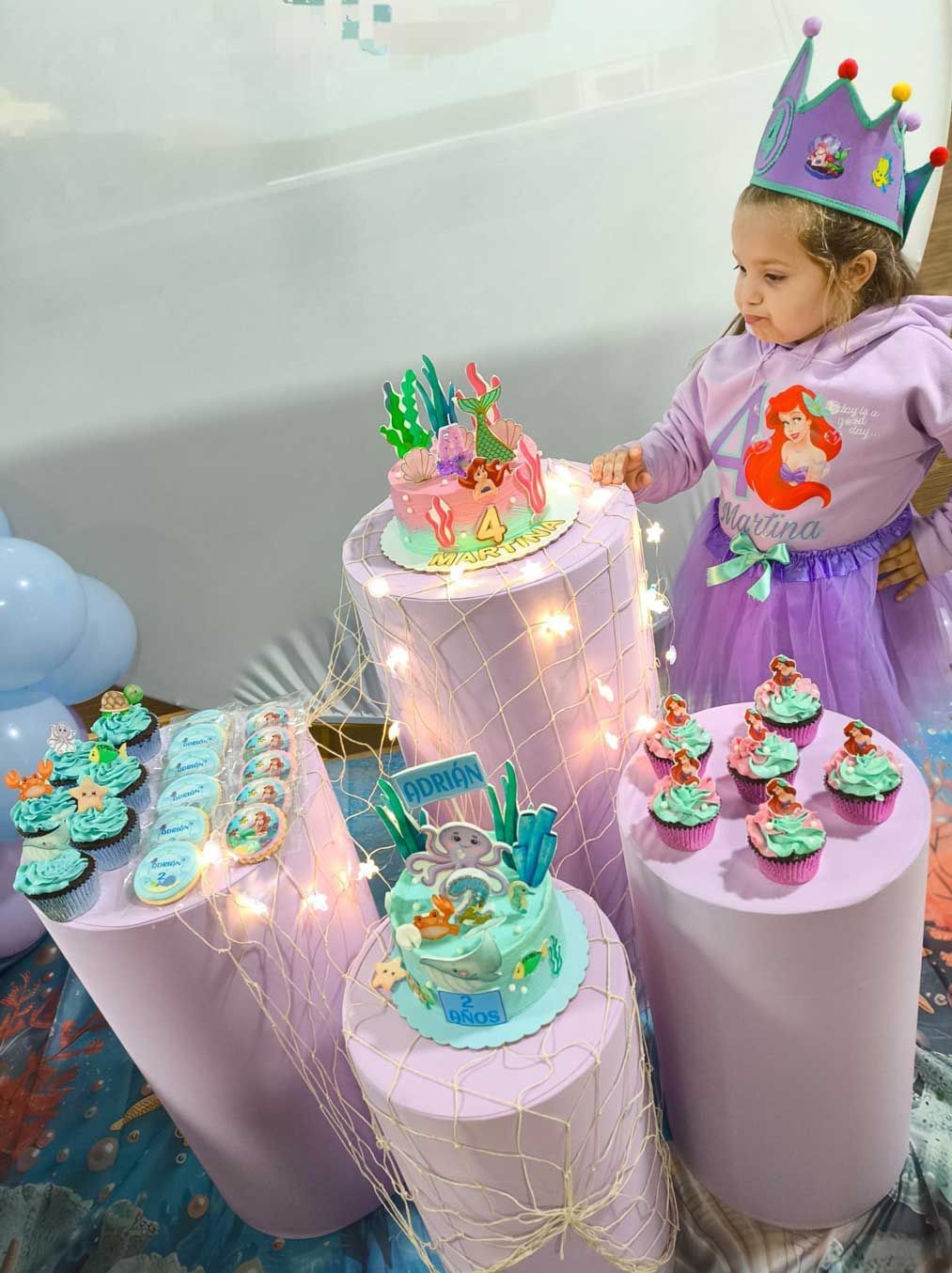 Una niña está parada frente a una mesa con pastelitos y pasteles.