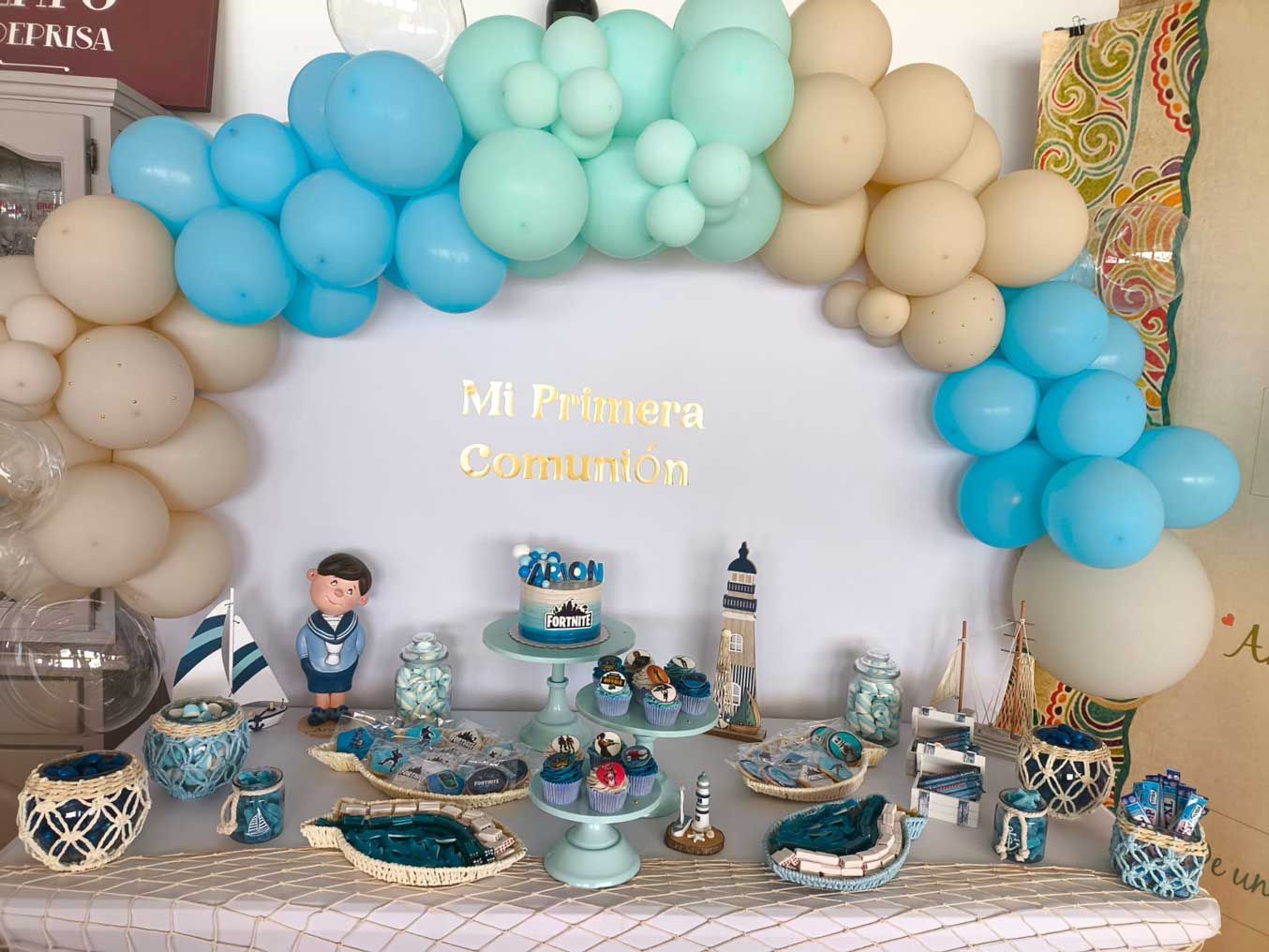 Una mesa decorada con globos azules y blancos para la primera comunión de un niño.