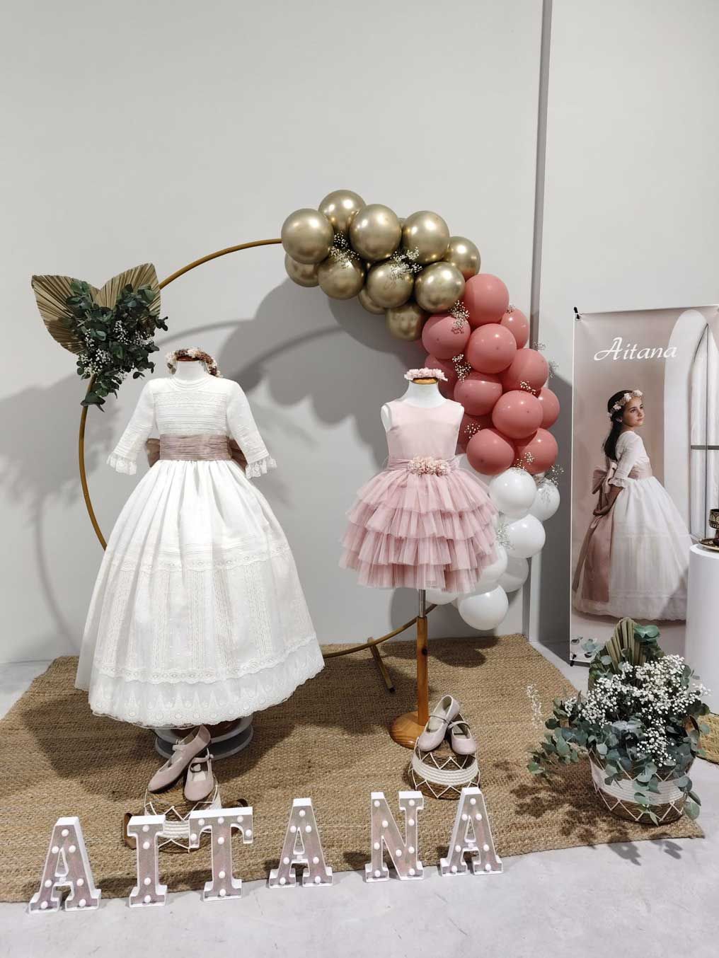 Una exhibición de vestidos para primera comunión con globos y flores.