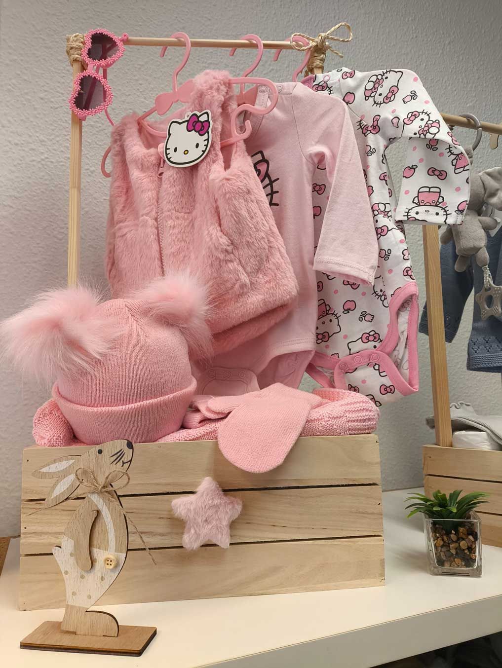 Una caja de madera llena de ropa rosa y un sombrero de Hello Kitty.