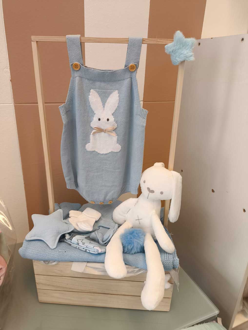 La ropa de un bebé y un conejito de peluche están en una cesta de madera.