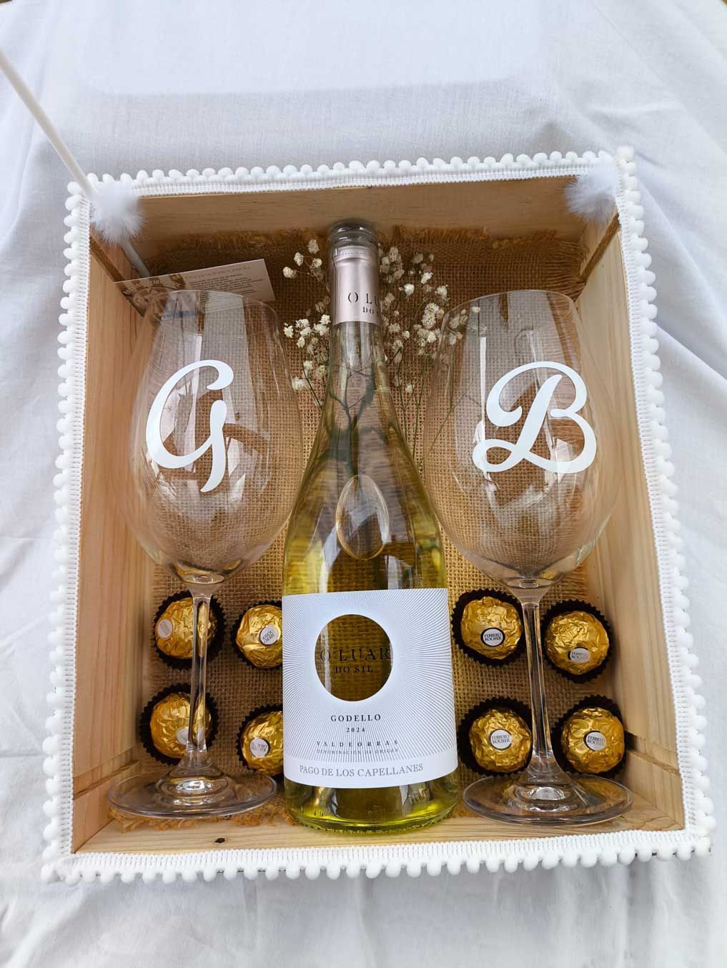 Una botella de vino, dos copas de vino y bombones en una caja de madera.