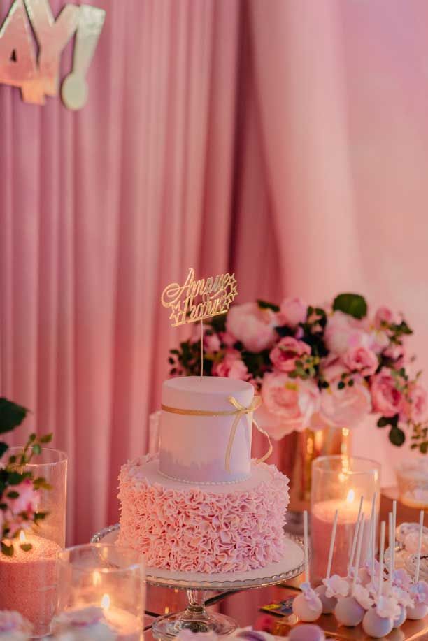 Un pastel rosa está sobre una mesa con velas y flores.